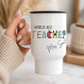 White mug with 'Worlds Best Teacher' text held by a hand on a light surface.