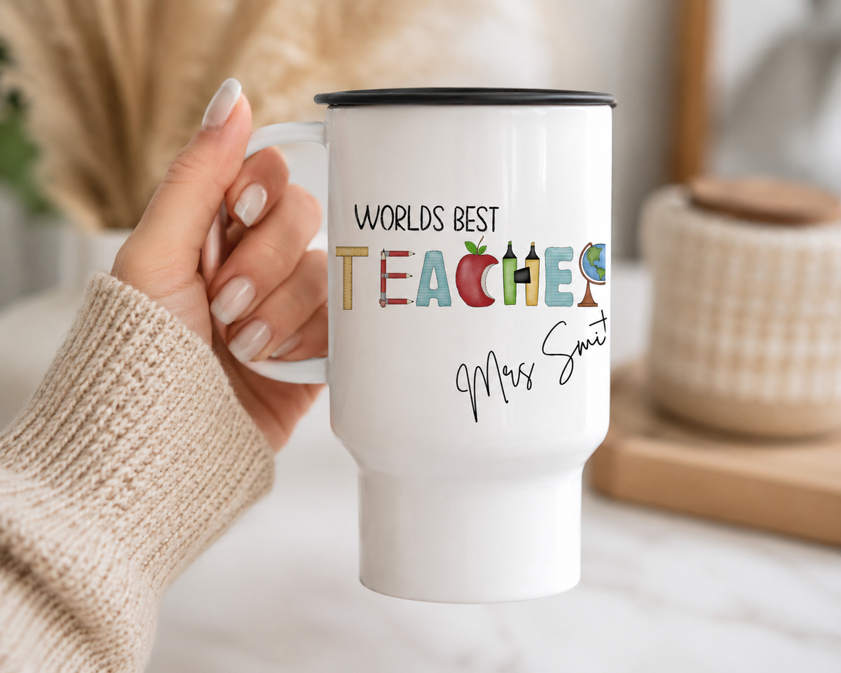 White mug with 'Worlds Best Teacher' text held by a hand on a light surface.